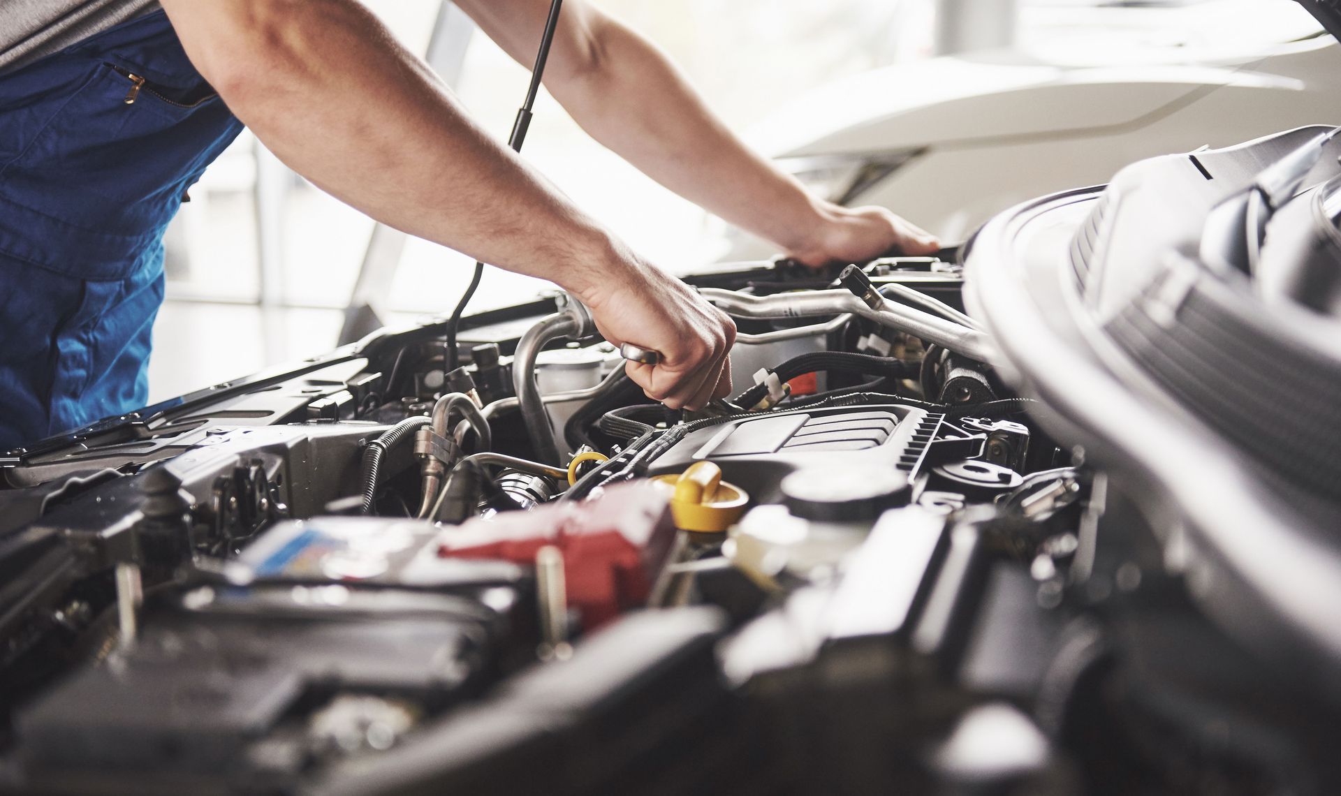 Mechanic working under an open car hood with tools in a garage