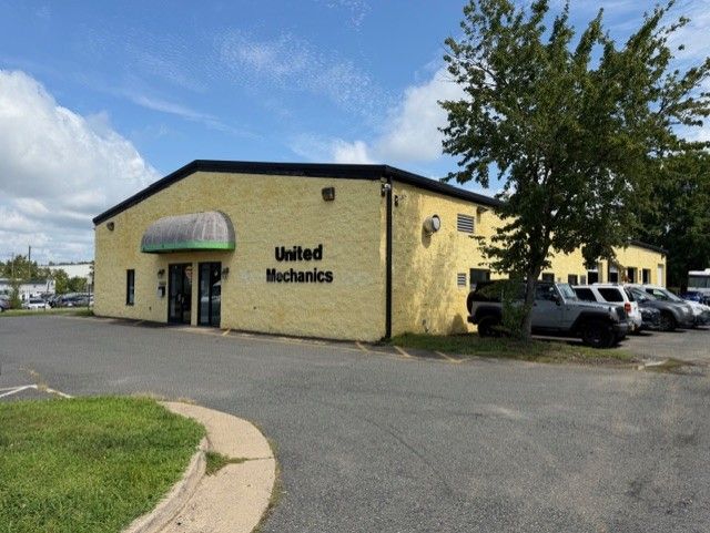 Yellow United Mechanics building with parked cars and a tree beside the lot