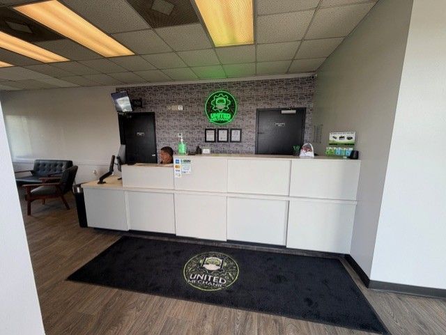 Empty lobby reception desk with black mats, white counter, and green circular logo on the wall