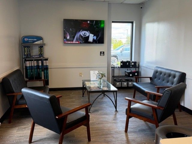 Small waiting room with blue chairs, glass coffee table, wall TV, and a window overlooking a parking lot