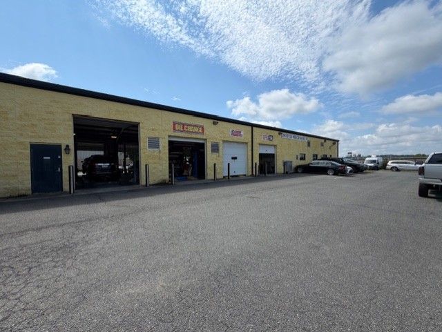 Yellow auto repair shop with open garage bays and parked cars under a partly cloudy sky