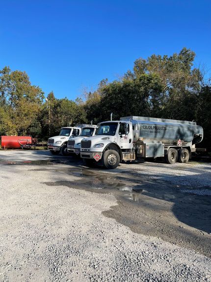 Two white utility trucks and a red tank parked on gravel under a clear blue sky