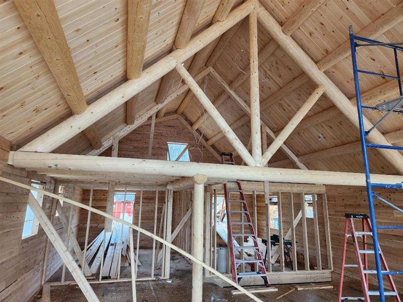 The inside of a log cabin under construction with a ladder in the foreground