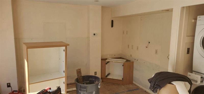 A room with a washer and dryer and a trash can in it.