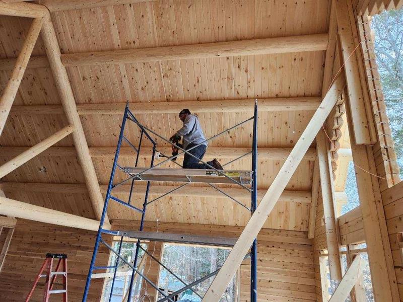 A man is kneeling on a scaffolding in a wooden building.