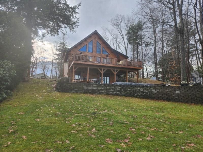 A large log cabin is sitting on top of a lush green hill surrounded by trees.