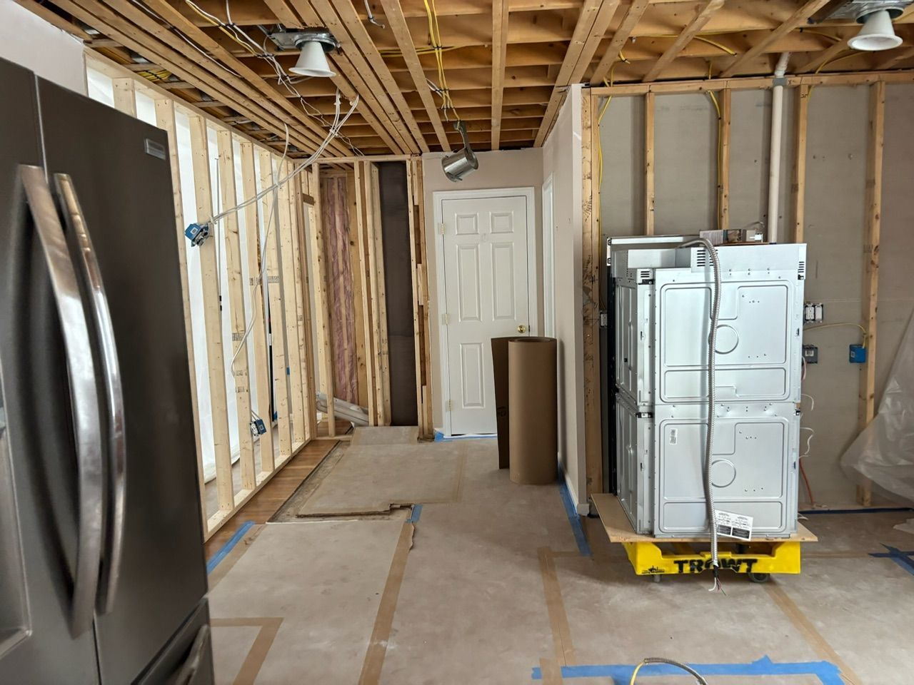 Partially renovated room with exposed framing, a stainless refrigerator, and a cabinet on a yellow dolly