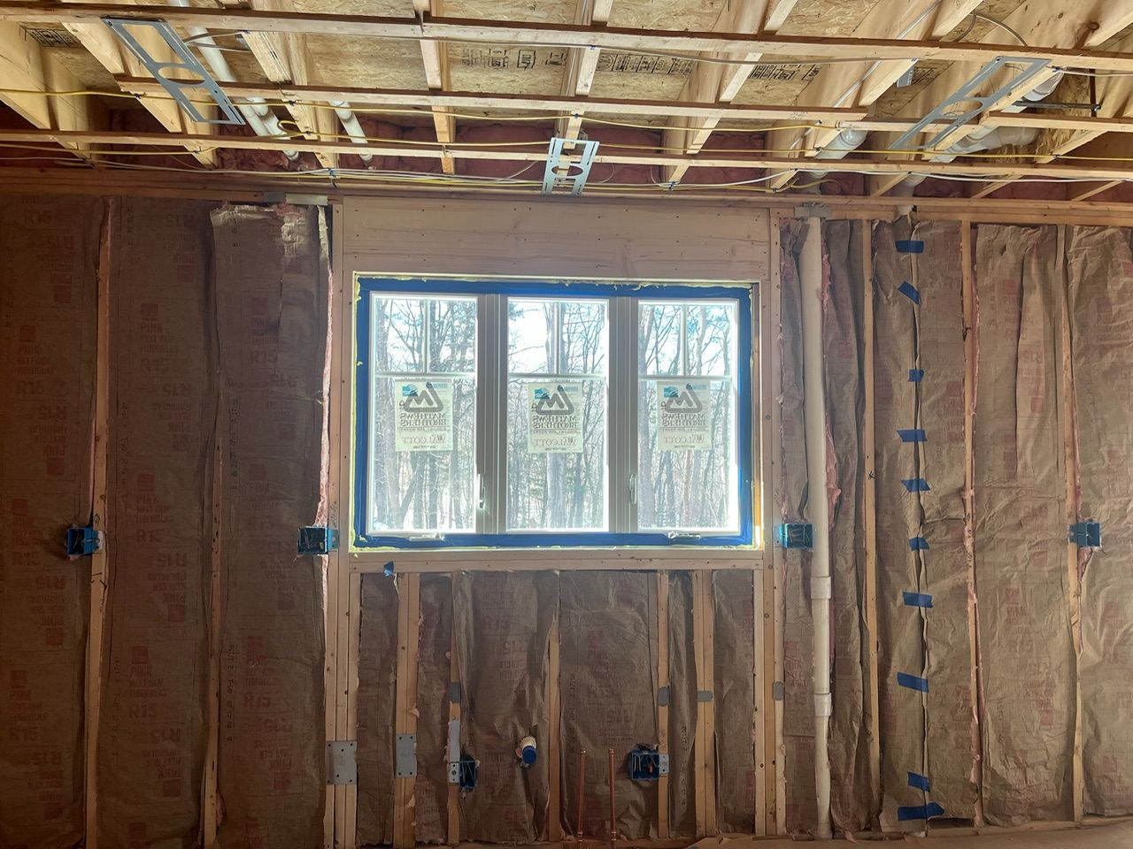 Unfinished room with exposed insulation and a centered window letting in daylight