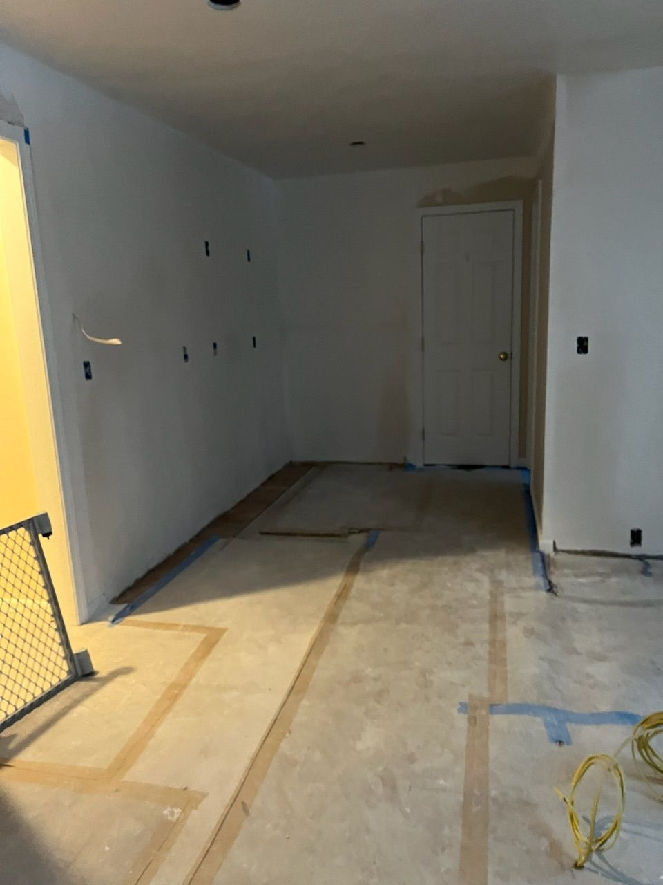 Empty unfinished room with white walls, bare floor, and a yellow safety barrier on the left.