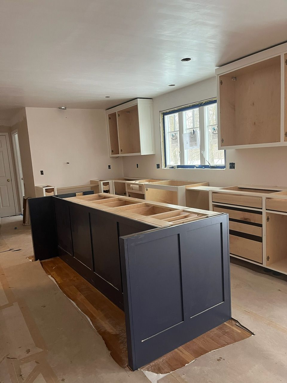 Kitchen under renovation with dark blue island, unfinished cabinets, and a window on the right
