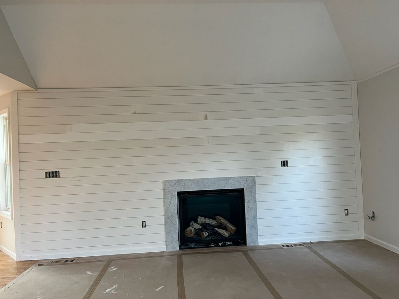 Empty living room with white textured walls, sloped ceiling, and a black fireplace centered on the far wall