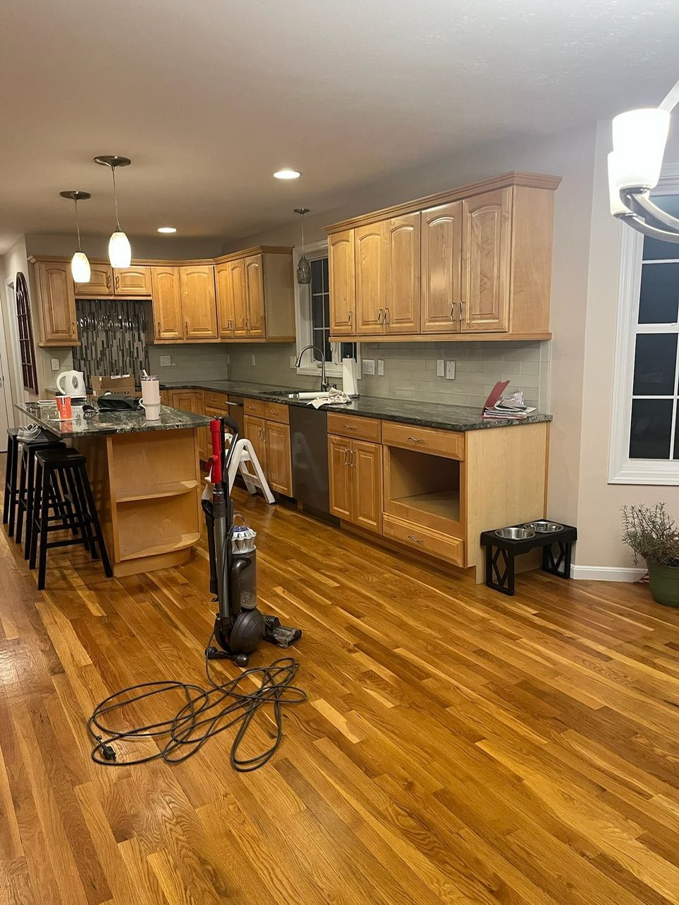 Kitchen with light wood cabinets, hardwood floors, and a vacuum cleaner in the center near a counter.