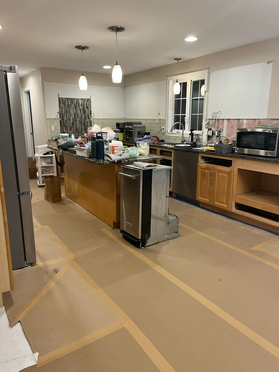 Messy kitchen with boxes, counters, and appliances on a covered floor during renovation