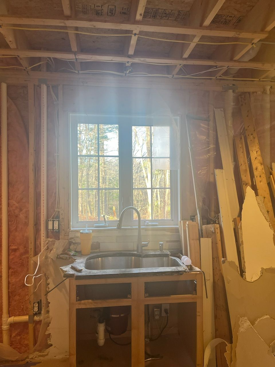 Partially renovated bathroom with exposed studs, a sink, and a window letting in bright light