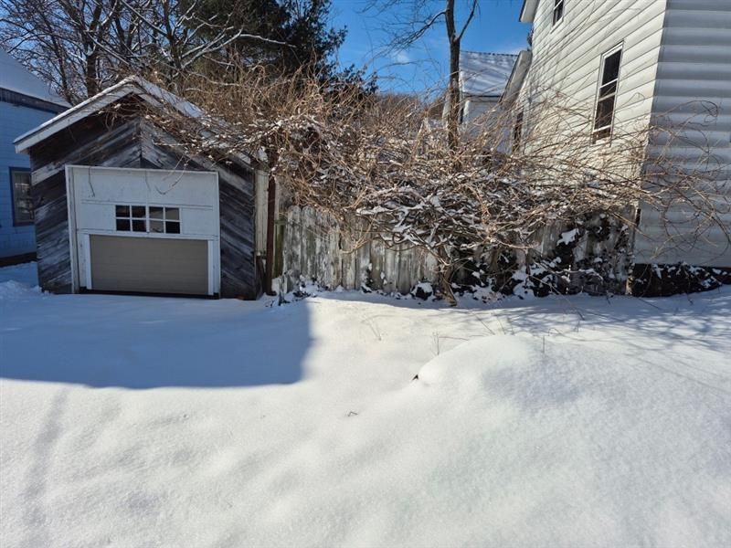 A snowy yard with a garage and a house in the background