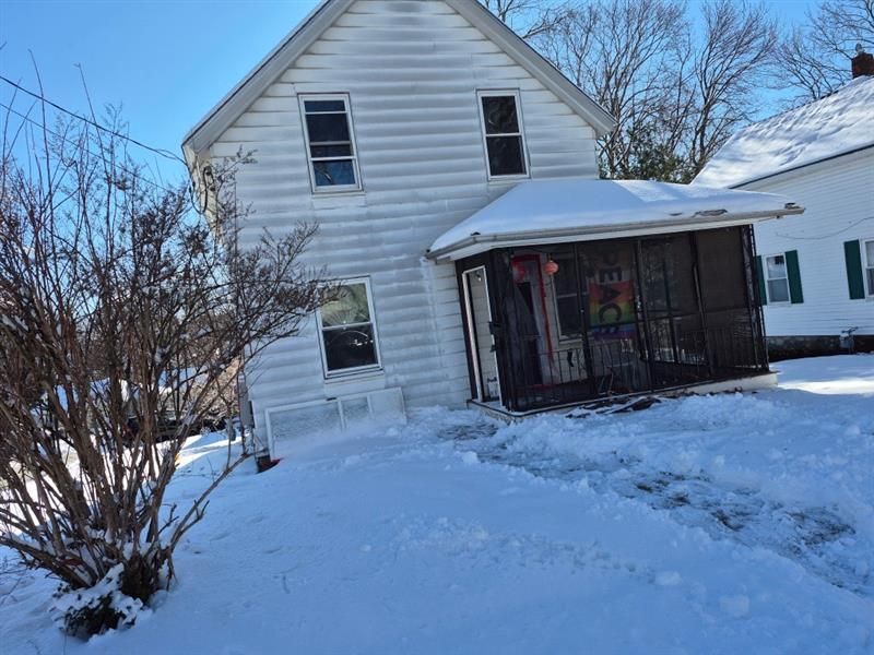 A white house with a screened in porch is covered in snow.