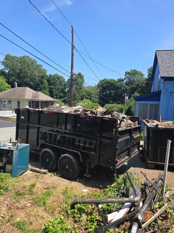 A dumpster filled with junk is parked in front of a house.