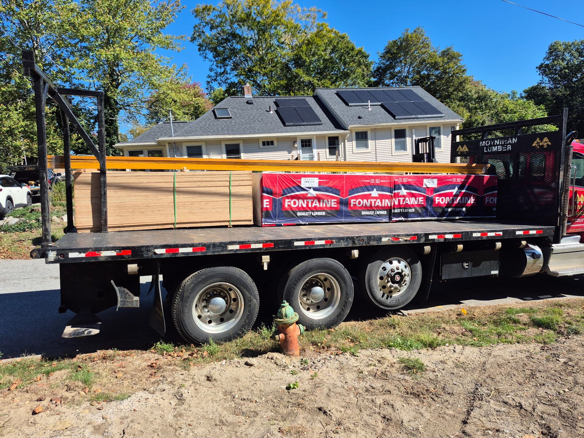 Flatbed truck loaded with lumber parked in front of a house.