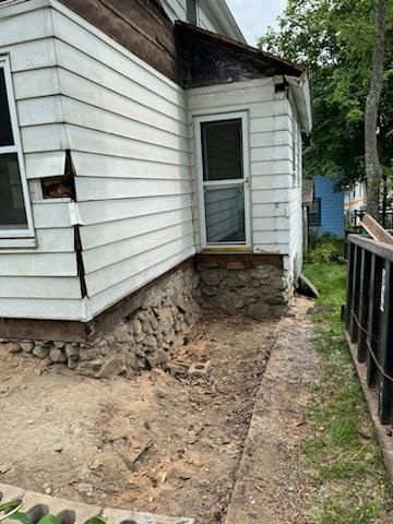 Exterior of a house with damaged siding, a stone foundation, and an accessible pathway.