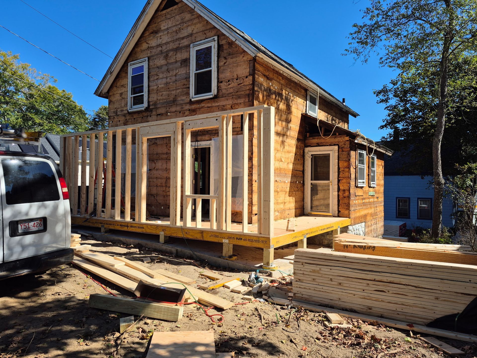 House under construction with exposed wooden frame and unfinished siding, sunny day.
