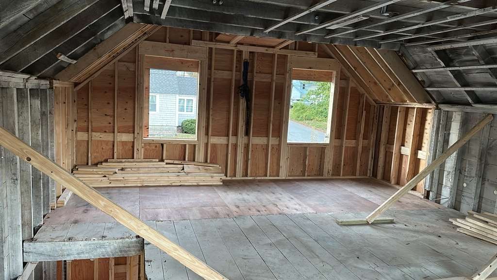Interior of a room under construction with framed walls, two windows, and a wooden floor.