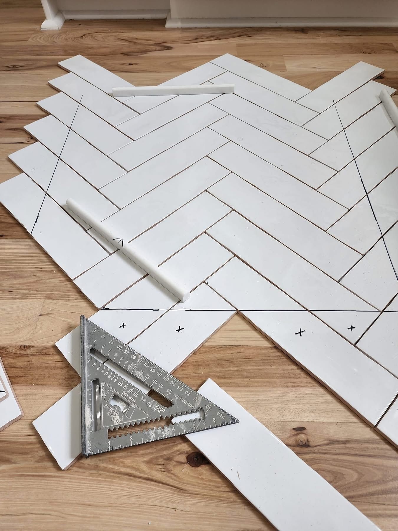 Herringbone tile layout with a speed square and pencil on a wooden floor.
