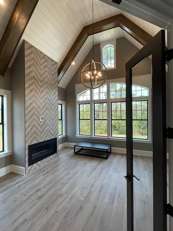 Interior room with fireplace and large windows, accented by a globe chandelier, hardwood floors, and wooden beams.