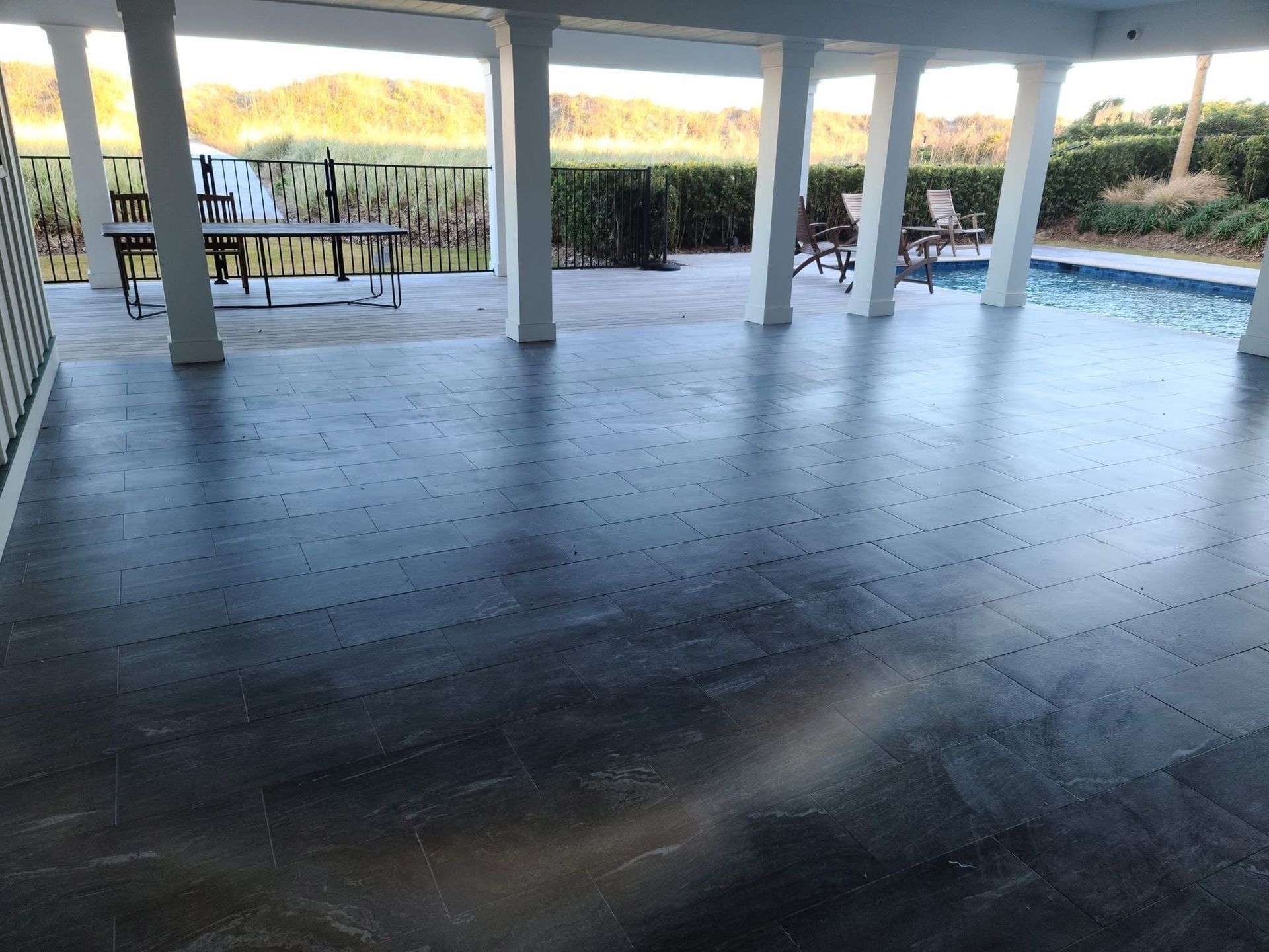 Covered patio with dark gray tiled floor, columns, table, and view of water.