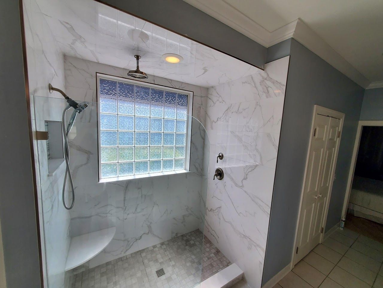 Marble-tiled shower with a glass block window, gray walls, and chrome fixtures.