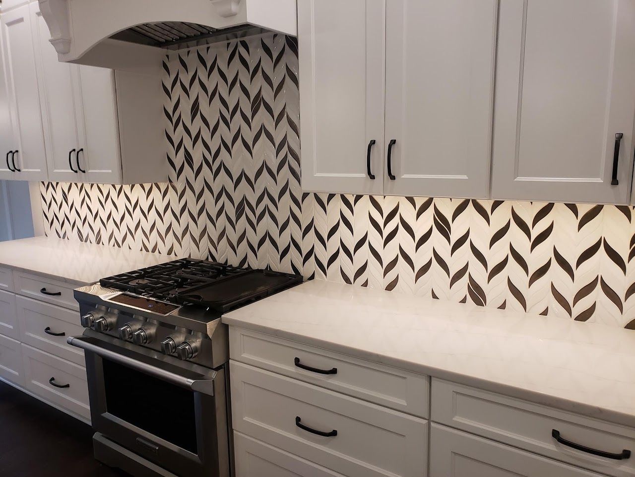 White kitchen with dark chevron backsplash, stainless steel oven, and black cabinet pulls.