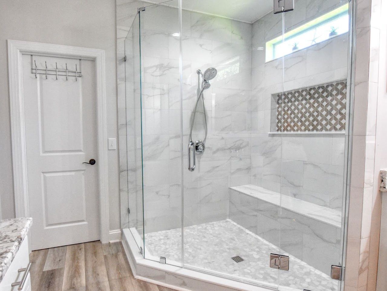 Modern shower with glass doors, white marble tiles, and built-in bench. Wooden floor.