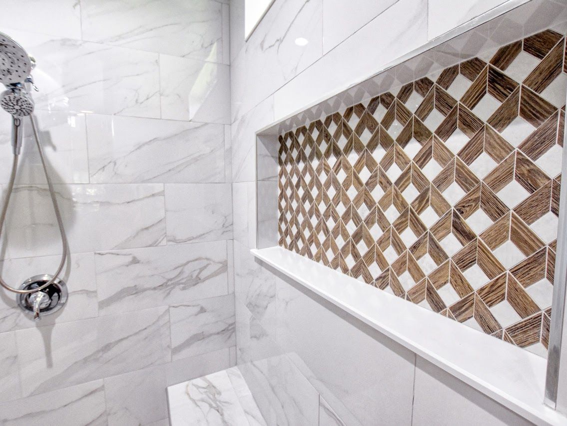 Shower interior with white marble tiles, built-in shelf with geometric wood-tone tile accent.