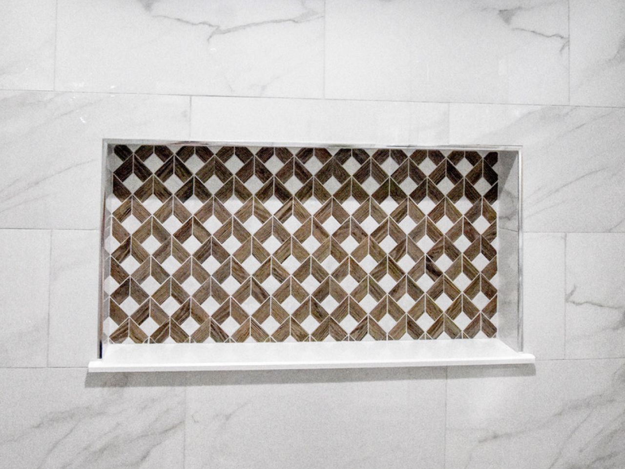 Shower niche with white frame, shelf, and patterned brown and cream tile.