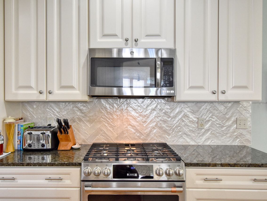Kitchen with stainless steel appliances, white cabinets, granite countertop, and textured backsplash.