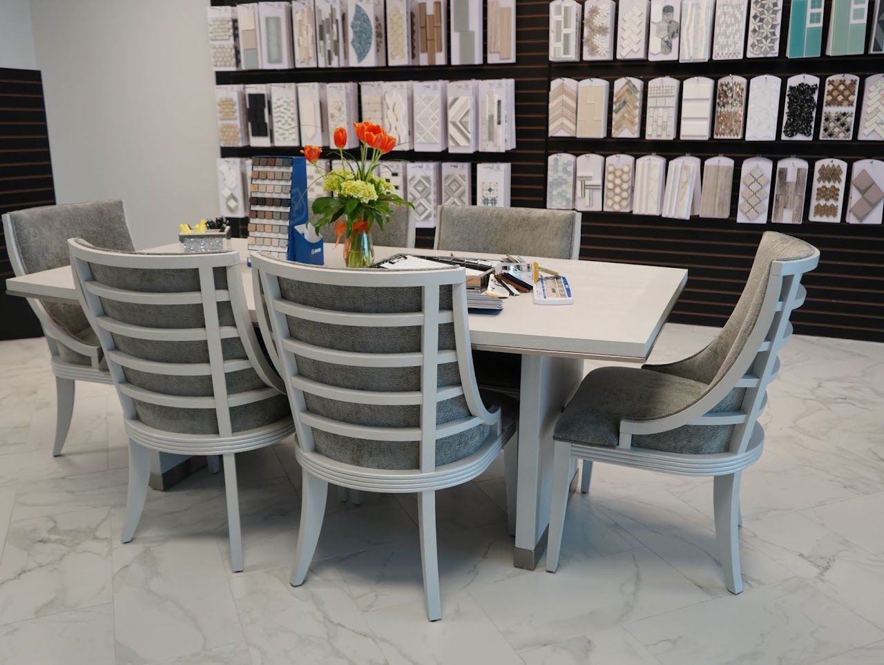 Dining room table set with six chairs. White table and chairs with gray cushions. Tile display in background.