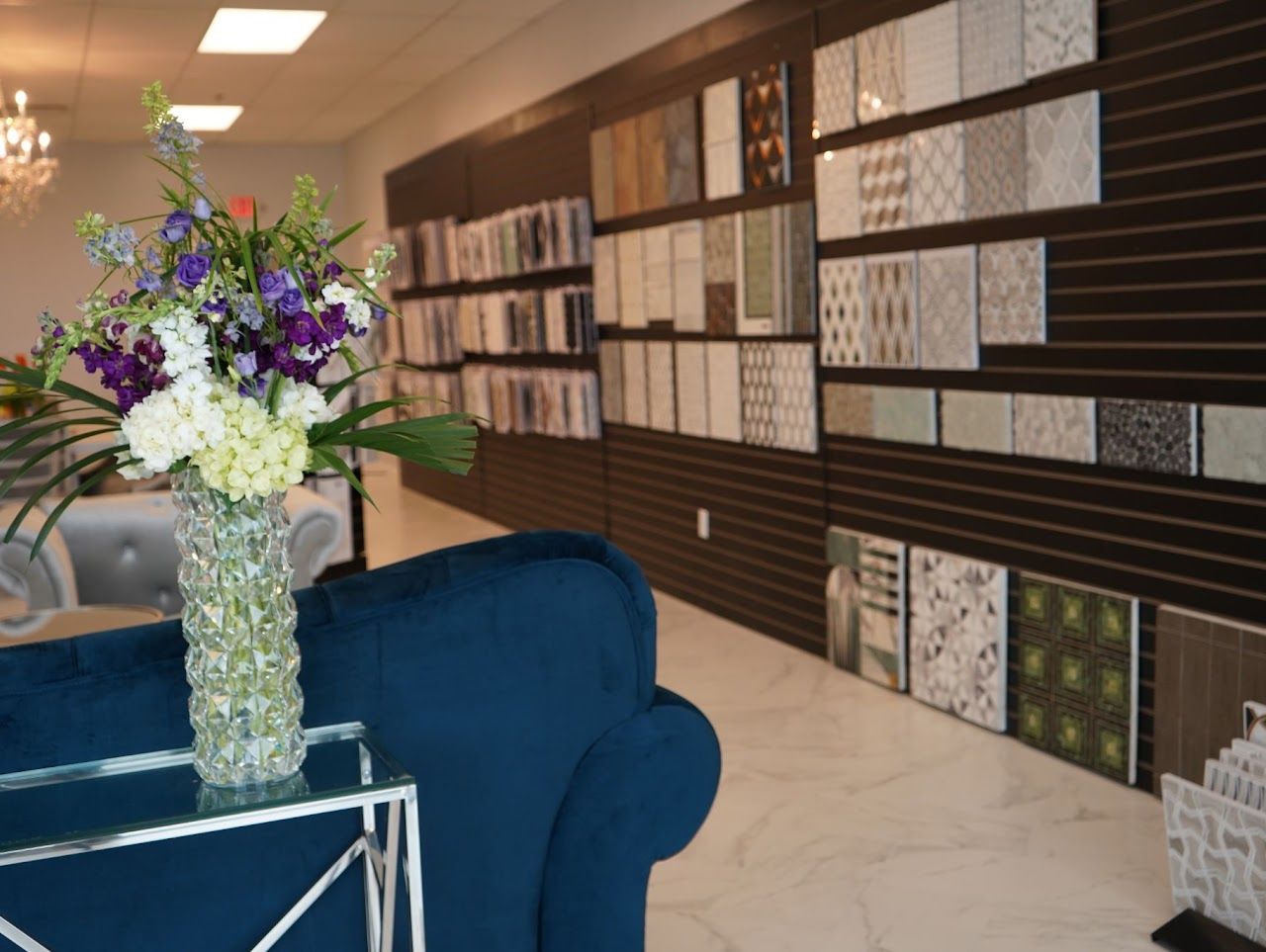 Tile showroom interior with tile samples on the wall, a vase of flowers, and a blue sofa.