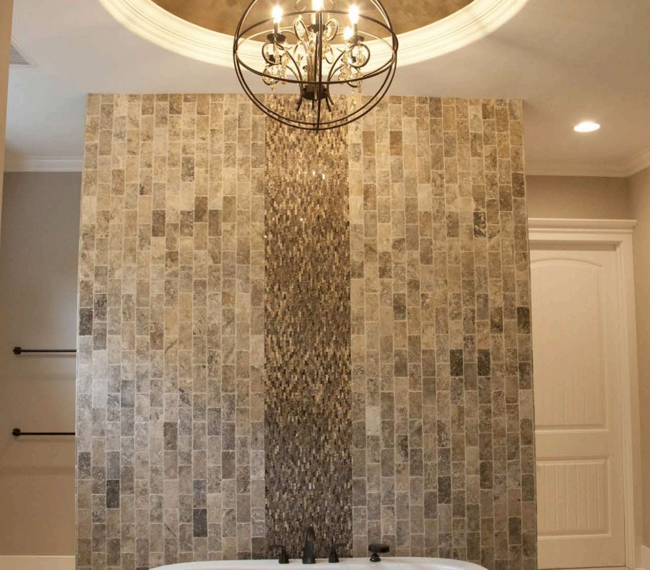 Bathroom with stone tile wall, central accent strip, chandelier, and white door.