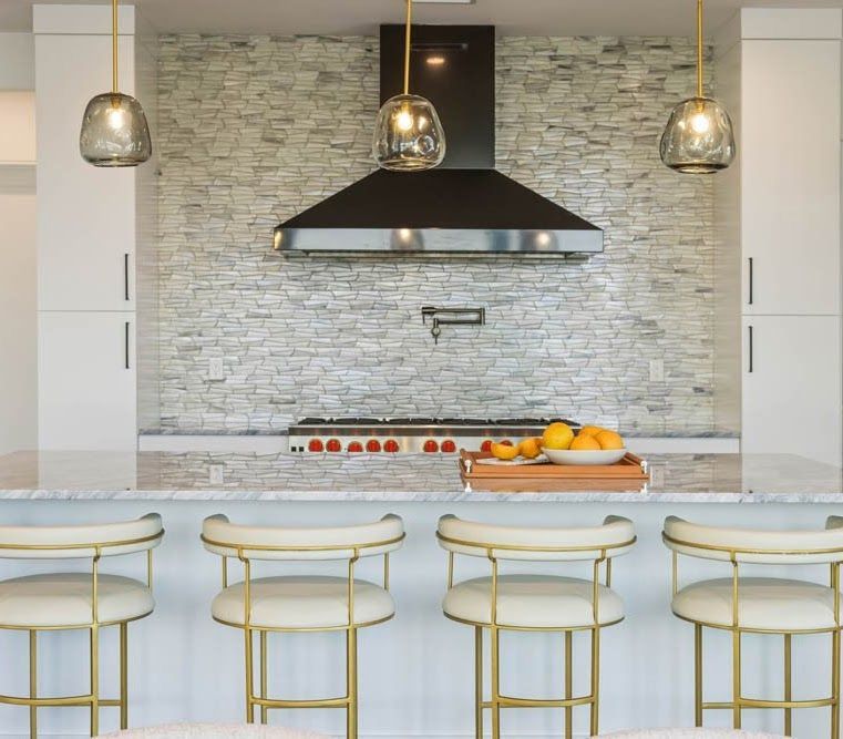 Modern kitchen with a white stone wall, stove hood, and gold bar stools.