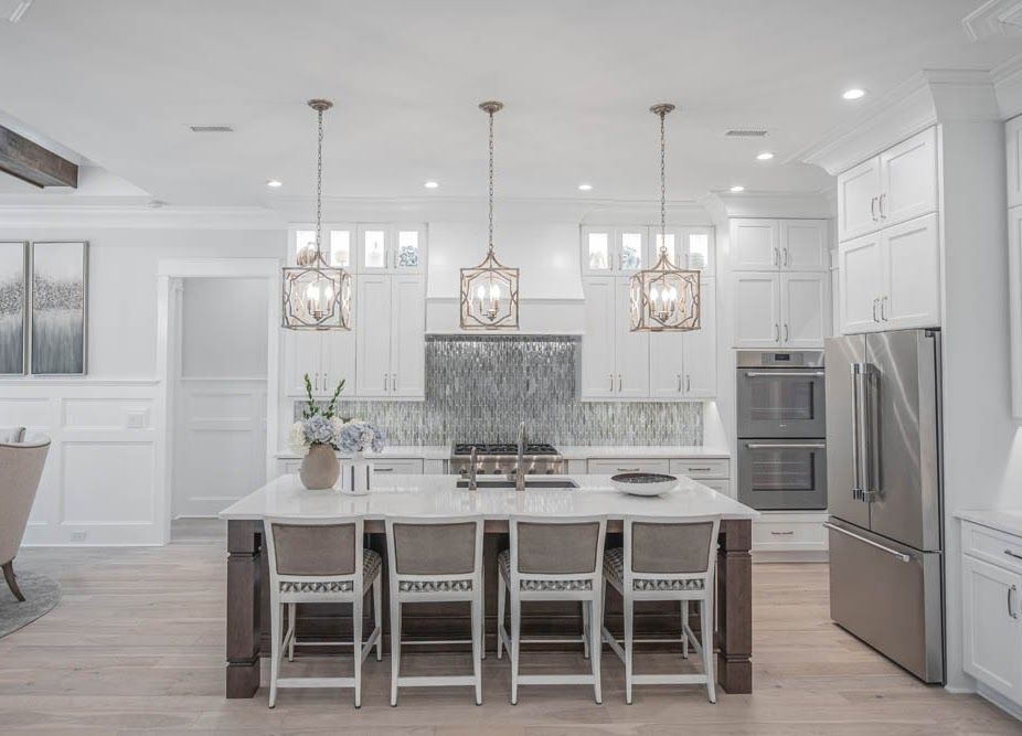 White kitchen with island, pendant lights, stainless steel appliances, and wood floors.