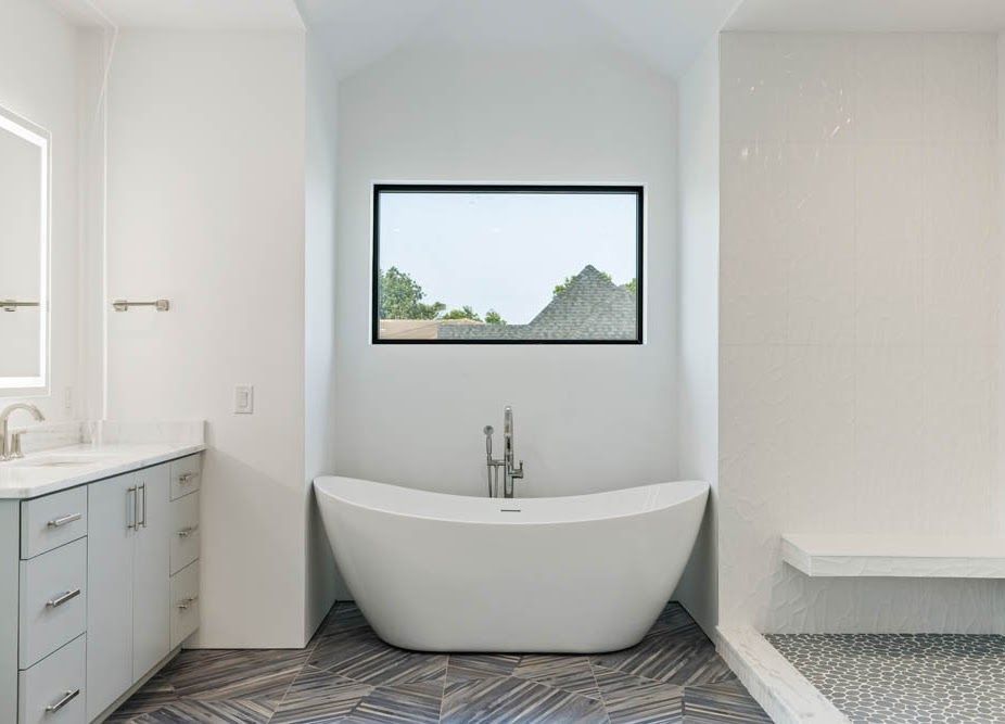 Modern bathroom with white tub, window, and vanity. Gray flooring and neutral walls.