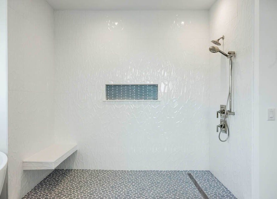 White tiled walk-in shower with gray pebble floor, built-in bench, and blue accent tile in the wall.