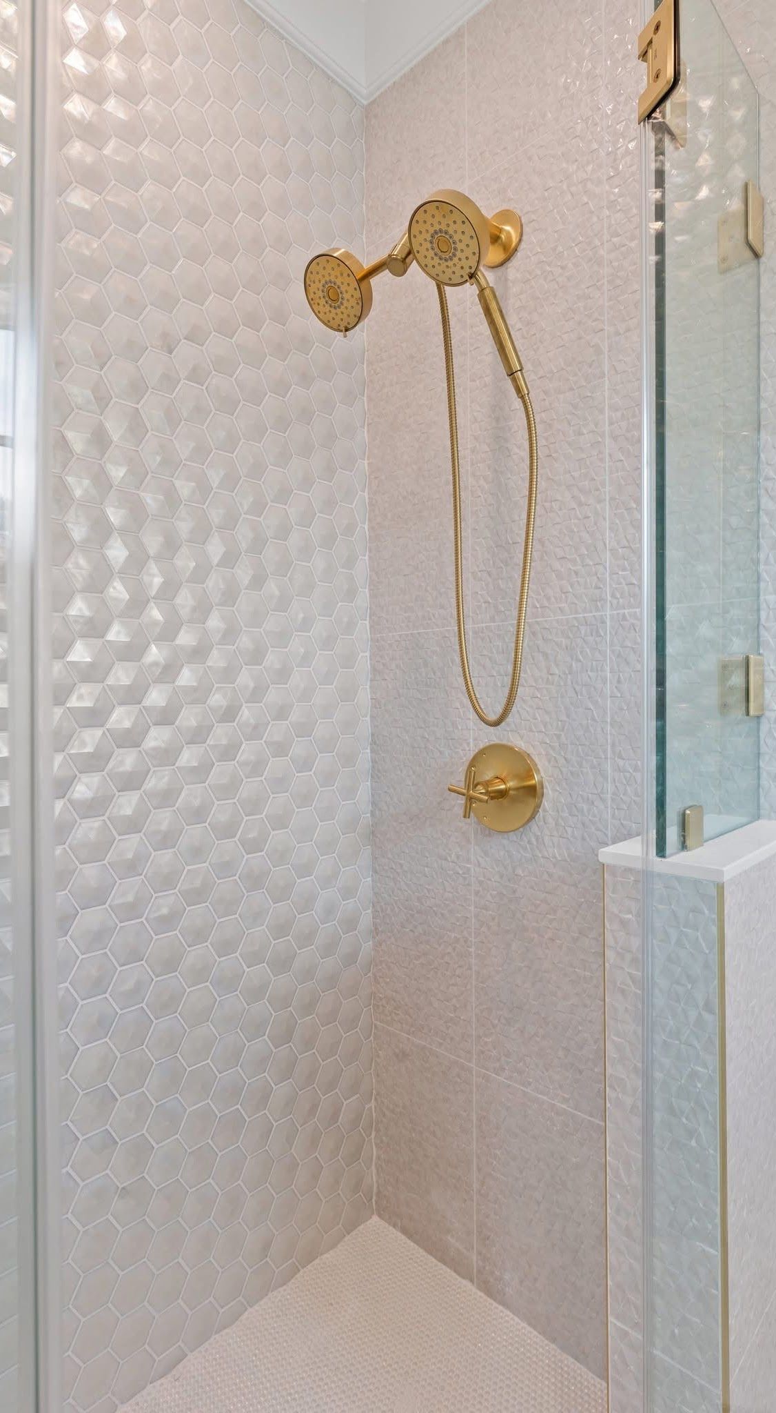 Shower with white textured tile walls, gold fixtures, and glass door.