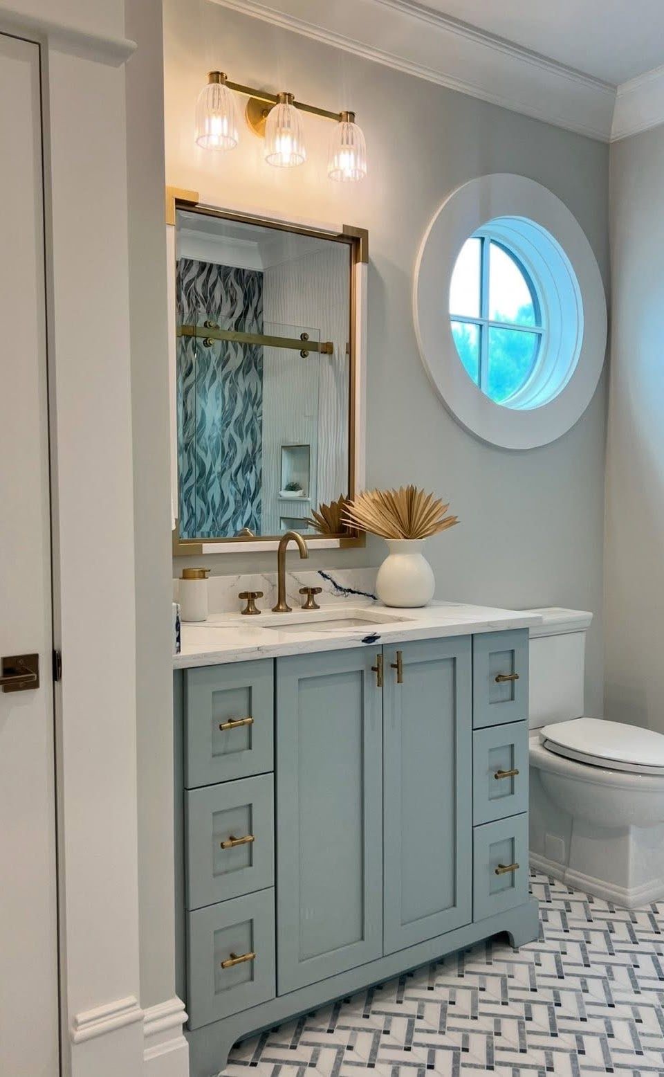 Powder blue vanity with gold accents, mirror, and round window in a bathroom.