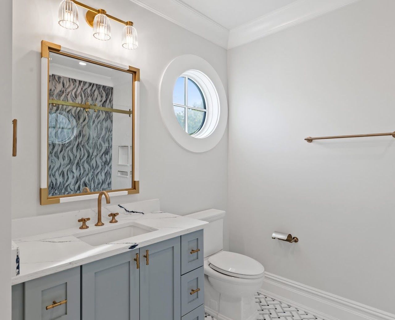 Bathroom with blue vanity, gold accents, round window, and patterned tile floor.