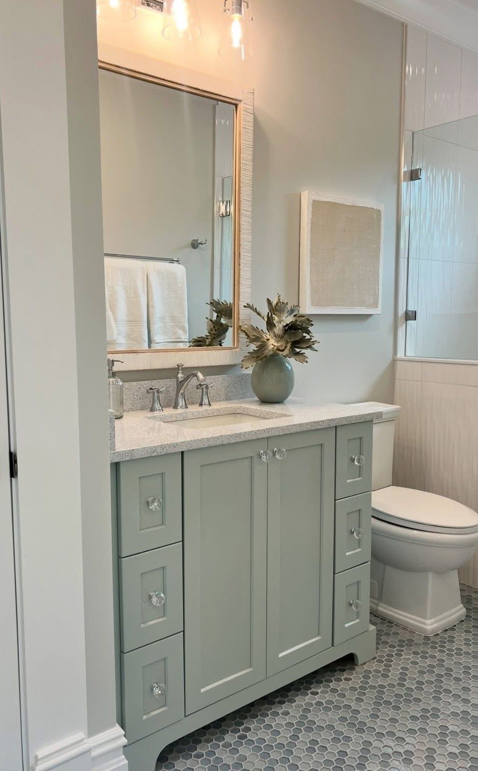 Green bathroom vanity with mirror, towels, and mosaic tile flooring.