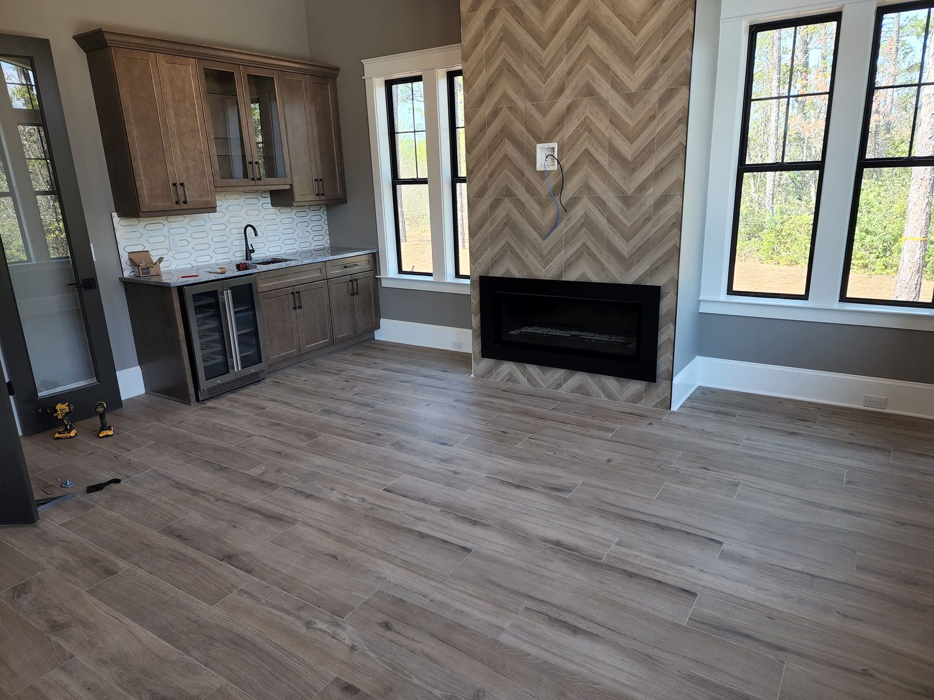 Living room with bar and fireplace; light wood floors, gray walls, light cabinets.