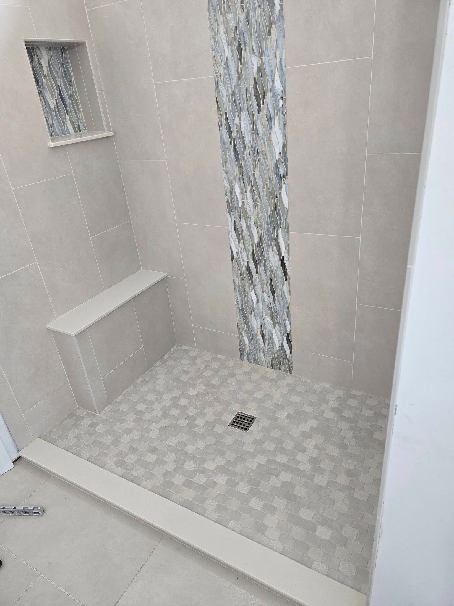 Completed shower with gray and beige tiles, built-in bench, and niche.
