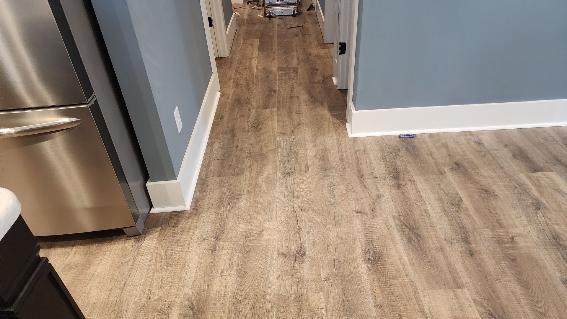 Hallway with wood-look flooring, blue walls, white trim, and a stainless steel refrigerator.