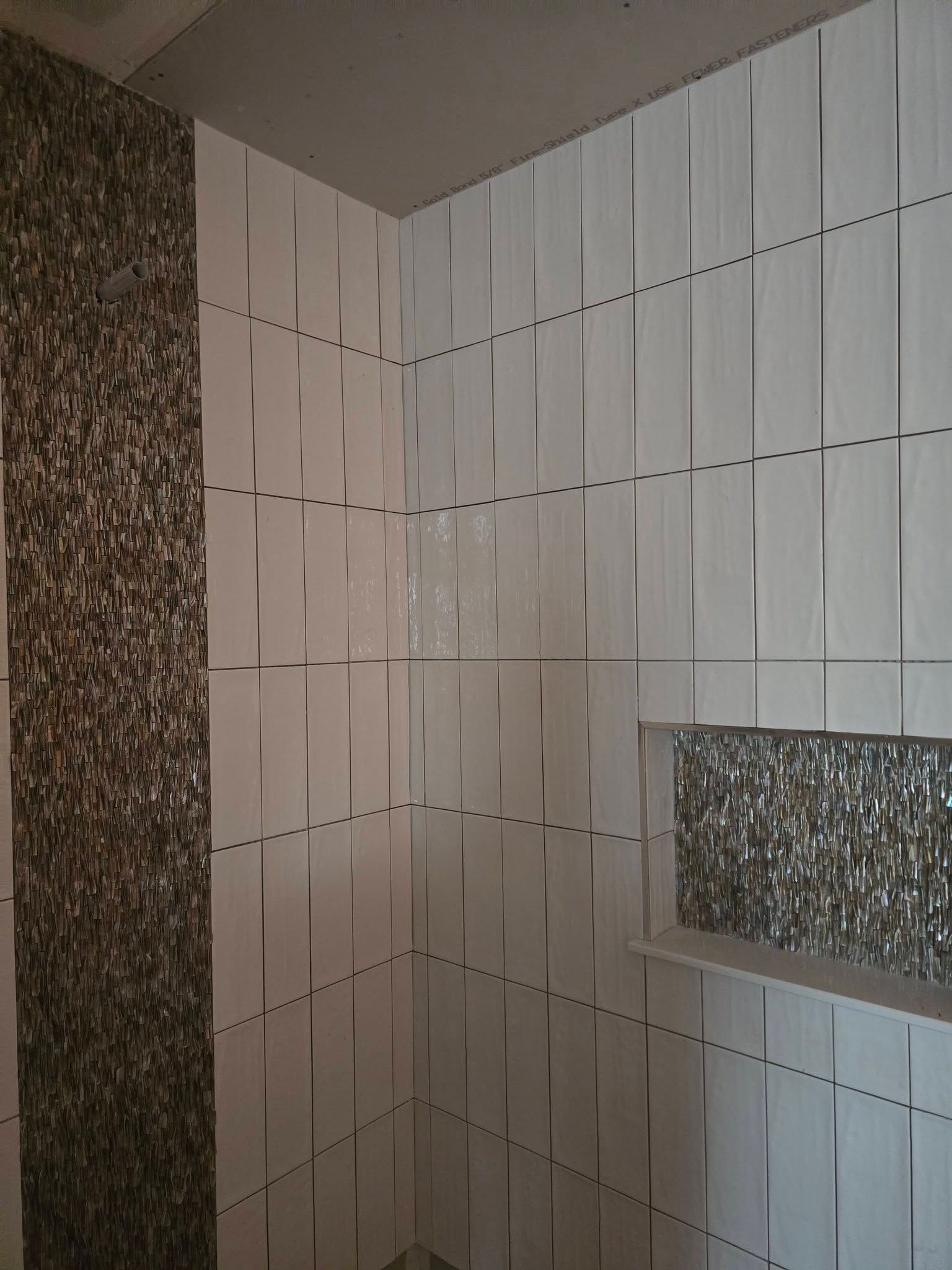 Tiled shower interior with white patterned walls, a textured accent strip, and a built-in shelf.