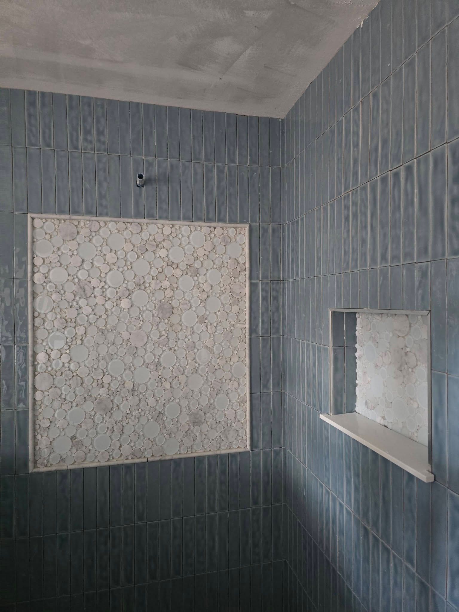 Blue tiled shower with a white, textured panel and a built-in shelf.